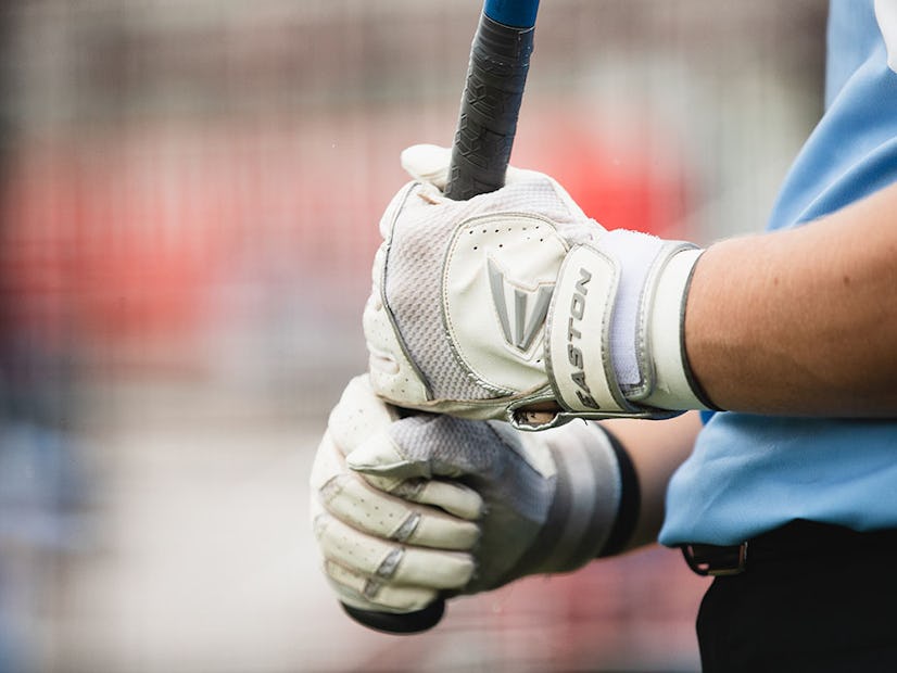 An athlete holding a bat with batting gloves on.