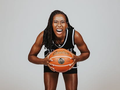 Ariel Atkins, wearing a black Athletes Unlimited basketball uniform, leans forward and cheers as she holds a basketball in both hands.