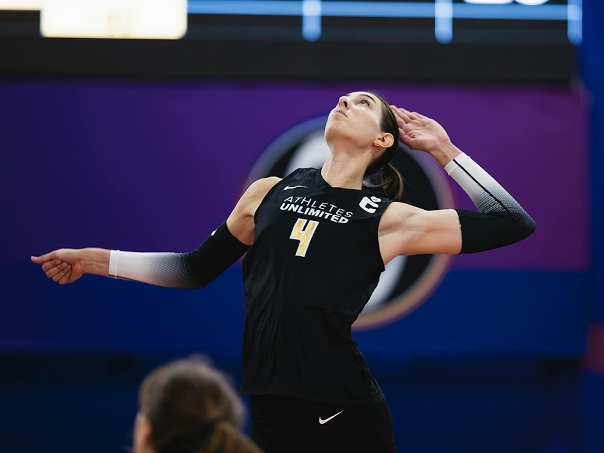 Brittany Abercombie, in her black Athletes Unlimited jersey, with white & black gradient arm sleeves, jumps and angles her arm back, ready to strike the Volleyball.