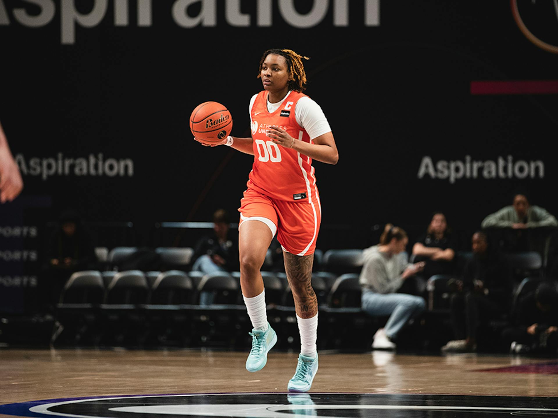 Alyssa Smith, wearing an orange Athletes Unlimited Pro basketball uniform with the jersey number 00 and white undershirt, white socks, and teal shoes, dribbles a basketball up the court.